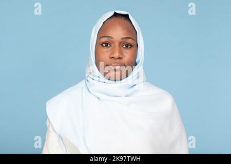 Ritratto di bella donna musulmana afro-americana in hijab posa su sfondo blu studio, primo piano Foto Stock
