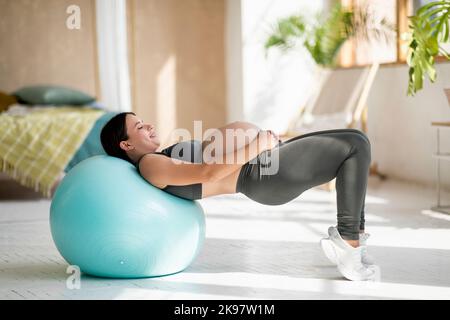 Donna incinta sportiva con Big Belly Training con Fitball a casa, Foto Stock
