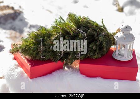 Scatole regalo rosse, albero di Natale con ghirlande, lanterna bianca su una soffice e bianca plaid all'aperto in inverno giorno nevoso. Sfondo festivo. Vacanze, regali, Foto Stock