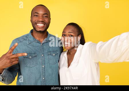 Sposi afroamericani che si posano facendo insieme Selfie su sfondo giallo. Foto Stock