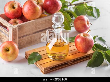 Aceto di sidro di mele in una bottiglia di vetro e mele fresche con foglie su sfondo chiaro Foto Stock