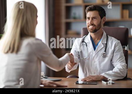 Medico maschile amichevole in mani di agitazione uniforme con paziente femminile Foto Stock