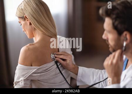 Controllo medico. Medico di sesso maschile che utilizza lo stetoscopio per controllare la respirazione di un paziente femminile, Foto Stock