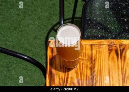 Un bicchiere alto di birra artigianale fredda con una spesse spesse spesse spuma di schiuma bianca. Il bicchiere di birra irlandese di birra di birra rossa si trova sul bordo di un tavolo di legno presso una fabbrica di birra. Foto Stock