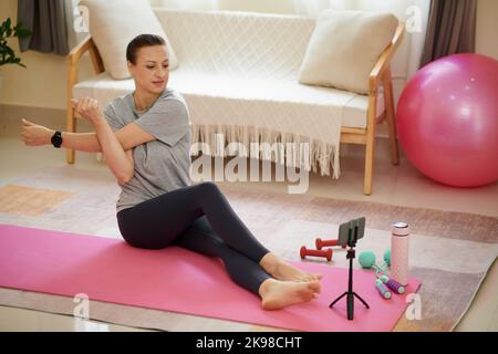 Donna che guarda i video di allenamento sullo smartphone e che fa esercizi di stretching Foto Stock