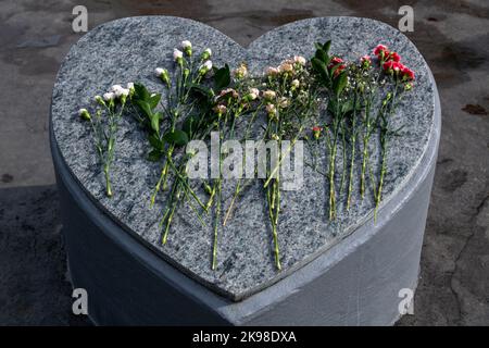 Una grande lapide grigia di granito a forma di cuore. Il monumento ha piccole macchie nere su di esso. La parte superiore e i lati sono lisci. Ci sono più lunghe st Foto Stock