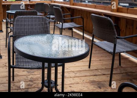 Più tavoli vuoti in metallo nero con piani di vetro rotondi e sedie in rattan nero su un patio caffè sul marciapiede di un ristorante all'aperto. Foto Stock
