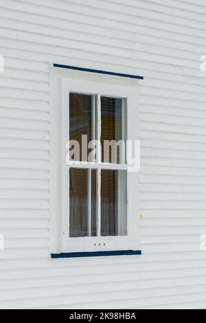 Una piccola finestra a cassettiera singola in uno stretto e bianco pannello di legno smussato che sida la parete esterna di una casa d'epoca. La finestra di vetro ha quattro riquadri. Foto Stock