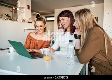 Tre donne che usano un computer portatile insieme mentre sono seduti in una caffetteria. Foto Stock