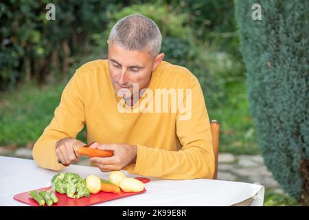 L'uomo caucasico fettine di carote per preparare gli ingredienti per l'insalata per cena all'aperto. Foto Stock