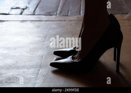 piedi femminili in scarpe nere con tacco alto sul pavimento a casa al buio, scarpe da donna, scarpe Foto Stock