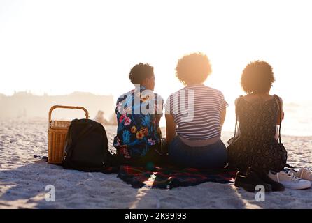 Gli amici sono tutto ciò di cui avete bisogno nella vita. Ripresa da dietro di un irriconoscibile trio di donne che hanno un picnic sulla spiaggia durante il giorno. Foto Stock