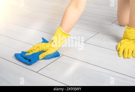 Servizio di pulizia. Le mani femminili nei guanti strofinano il pavimento bianco con un panno in microfibra blu. Pulizia dei pavimenti. Pulizia e manutenzione dei pavimenti in legno duro Foto Stock