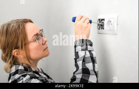 Donna con cacciavite che ripara una presa elettrica. Donna che installa una presa elettrica in casa, manutenzione della spina elettrica. Lavoro pericoloso con Foto Stock