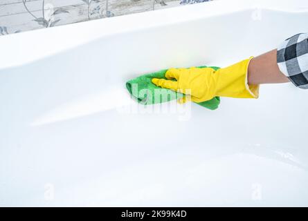 Primo piano pulizia mani bagno acrilico bianco. Servizio di pulizia mani in croped indossare guanti gialli proteggere con panno verde pulizia bagno acrilico bianco, Foto Stock