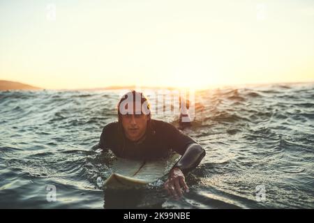 Vita migliore quando youre surfing. Un giovane uomo che paddling su una tavola da surf nel mare. Foto Stock