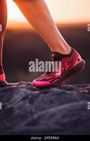 L'escursionista è salire sulle pietre con running, scarpe sportive, tramonto, primo piano Foto Stock
