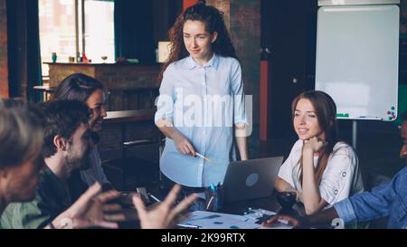 Il leader del team femminile sta parlando con il suo team multietnico discutendo la strategia aziendale nell'ufficio loft di un'azienda internazionale. Discussione, giovani, spazio di lavoro e concetto di pianificazione. Foto Stock