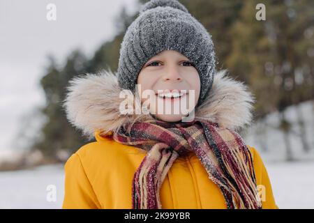 Primo piano ritratto di carino bambino di 8 anni sullo sfondo del paesaggio invernale. Ragazzo sorridente in abiti caldi che si divertono all'aperto. Concetto di christma Foto Stock