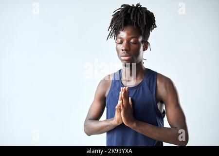 Ritratto di giovane africano meditando con gli occhi chiusi in piedi su sfondo blu Foto Stock