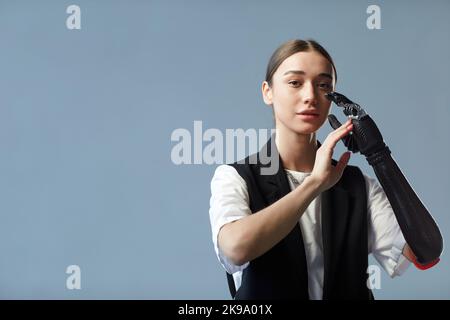 Ritratto di giovane donna con braccio protesico guardando la telecamera in piedi su sfondo blu Foto Stock