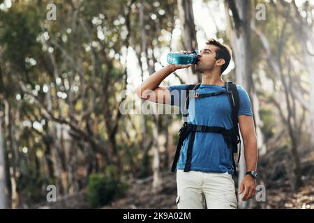 Un giovane spensierato che beve acqua da una bottiglia mentre va per un'escursione su una montagna. Foto Stock