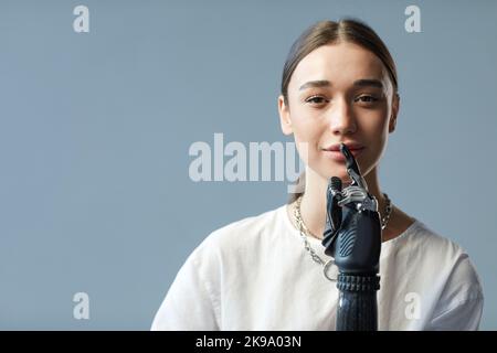 Ritratto di giovane donna con disabilità con braccio protesico guardando la telecamera su sfondo blu Foto Stock