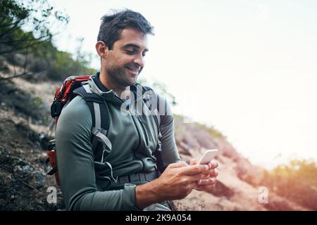 Im ha stupito che i theres segnalano qui. Un giovane uomo allegro che SMS sul suo cellulare mentre andando per un'escursione su una montagna. Foto Stock