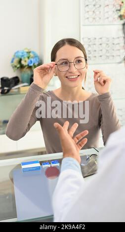 Una giovane donna piacevole che prova nuovi occhiali con optometrista al negozio ottico. Visione e concetto di visione Foto Stock
