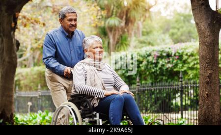 HES è sempre stata la mia principale fonte di sostegno: Un uomo anziano affettuoso che spinge la sua sedia a rotelle per far girare la moglie intorno al parco. Foto Stock