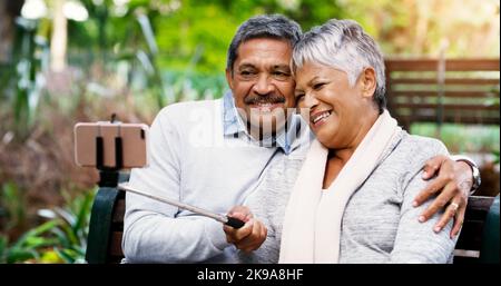 Abbiamo ancora un bell'aspetto come sempre. Una coppia affettuosa e anziana che usa un cellulare per prendere un selfie insieme nel parco. Foto Stock
