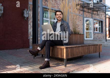 Un giovane uomo siede su una panchina con un notebook e guarda via, principi e regole di successo del concetto di business Foto Stock