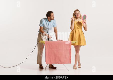 Ritratto dell'uomo che stira mentre la bella donna che fa il suo trucco isolato su sfondo bianco Foto Stock