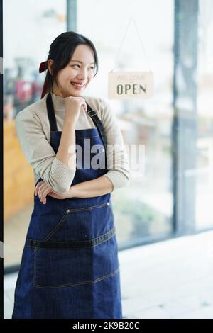 Iniziando e aprendo una piccola impresa, una giovane donna asiatica che mostra un volto sorridente in un grembiule in piedi di fronte al banco del bar della caffetteria. Business Foto Stock