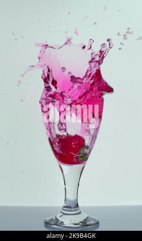 Frutta che si spruzzi nel vino, nello spirito, nel bicchiere da cocktail, nella splendida cornice gelata di vivaci gocce d'acqua liquida rosa sparse nell'aria per bar, feste, pub. Foto Stock