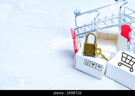 Carrello per la spesa in miniatura rovesciato con scatole di consegna etichettate e lucchetto con chiave. Concetto di privacy dello shopping online. Foto Stock