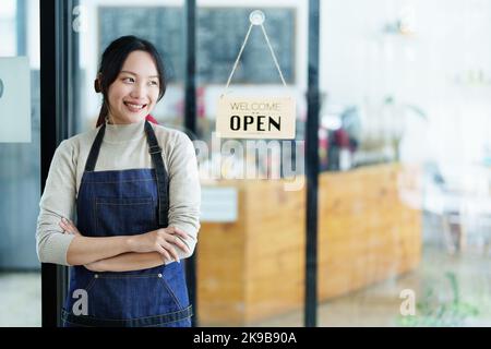 Iniziando e aprendo una piccola impresa, una giovane donna asiatica che mostra un volto sorridente in un grembiule in piedi di fronte al banco del bar della caffetteria. Business Foto Stock