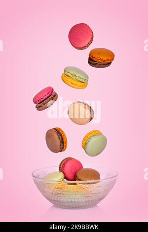 Macaron volanti che cadono in un piatto d'annata su sfondo rosa Foto Stock