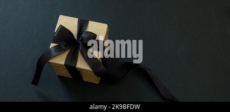 Banner di vendita del Black Friday. Confezione regalo con nastro nero isolato su sfondo nero, spazio copia. Natale presenta concetto. Foto Stock