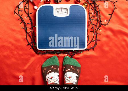 Una donna sta andando levarsi in piedi sulla bilancia su uno sfondo rosso, peso dopo le feste di Natale Foto Stock