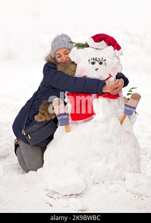ragazza che abbraccia un pupazzo di neve. tema invernale - ragazza che abbraccia un pupazzo di neve all'aperto Foto Stock