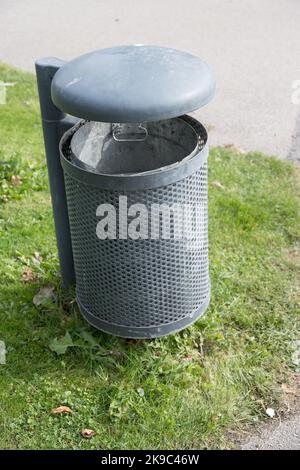 Primo piano dei rifiuti di metallo massiccio può spazzare la polvere con il coperchio posizionato sulla superficie erbosa nel parco pubblico come concetto per l'ambiente pulito e le aree pubbliche Foto Stock