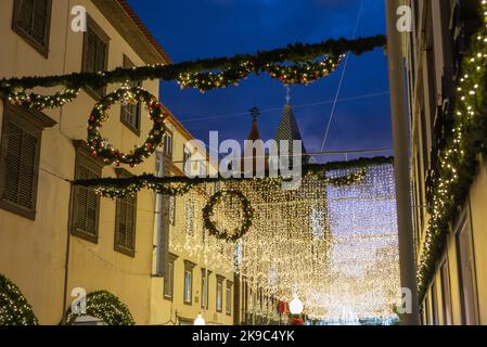 Un sacco di decorazioni natalizie con luci che pendono sulle strade da casa a casa e un cielo scuro sullo sfondo. Foto Stock