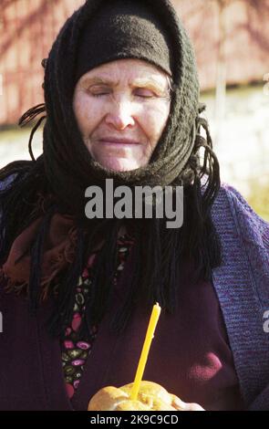 Gorj County, Romania, circa 2000. Donna anziana con pane e un'elemosina data per l'anima di un morto. Costume religioso in Romania. Foto Stock