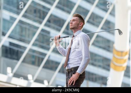 Riuscito giovane cuacasion uomo d'affari sicuro del CEO che indossa la camicia bianca con il randello di golf nella città che guarda in su nel cielo con Dreamy. Foto Stock