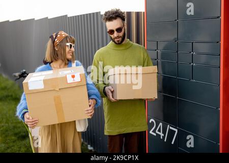 L'uomo e la donna trasportano pacchi ricevuti in macchina automatica posta all'aperto Foto Stock