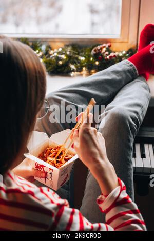 Donna che mangia fast food da takeaway scatola cinese tagliatelle asiatiche con verdure in wok scatola utilizzando bacchette. Consegna di alimenti senza contatto. Ragazza che gode T Foto Stock