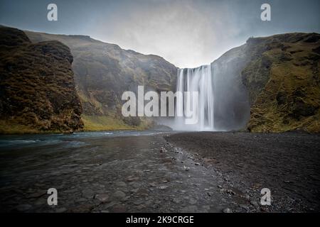 La maestosa cascata di Skógafoss (Skogafoss) si getta in un fiume tra le scogliere colorate dell'Islanda meridionale. Foto Stock