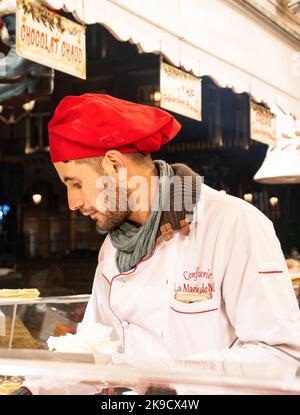 PARIGI, FRANCIA - 6 GENNAIO 2019: Venditore in cappello rosso Santa chef prepara e vendite tradizionali waffle freschi e crepes al mercato di Natale durante la wint Foto Stock
