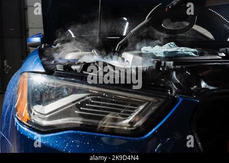 Lavaggio a vapore del motore di auto nei dettagli del servizio auto. Processo di pulizia a vapore del motore dell'auto da polvere e sporcizia Foto Stock
